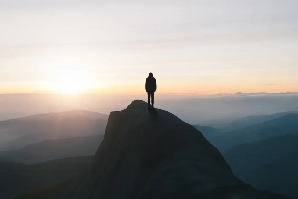 A person demonstrating an Unbreakable Mindset Method and mental resilience by standing on a mountain peak at sunrise.