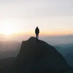 A person demonstrating an Unbreakable Mindset Method and mental resilience by standing on a mountain peak at sunrise.